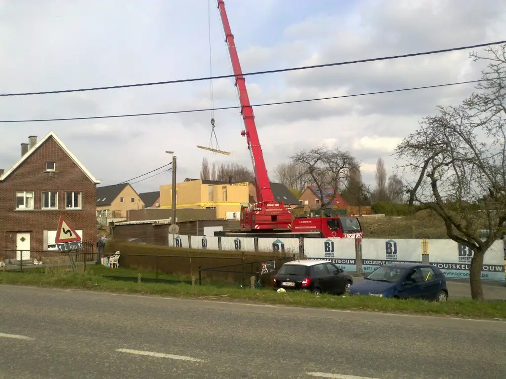 een houtskeletbouw in aanbouw met een grote kraan en werfdoeken van BJ concept