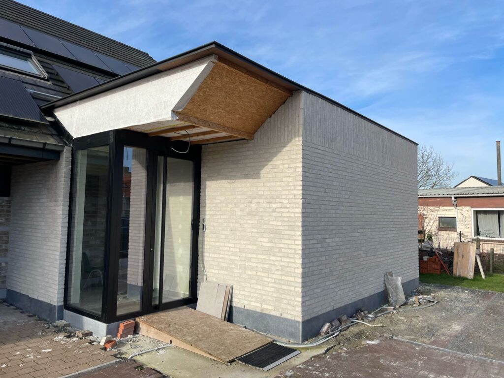 Aanbouw in Merelbeke met lichte gevelsteen en glazen inkom, vóór de afwerking van de luifel