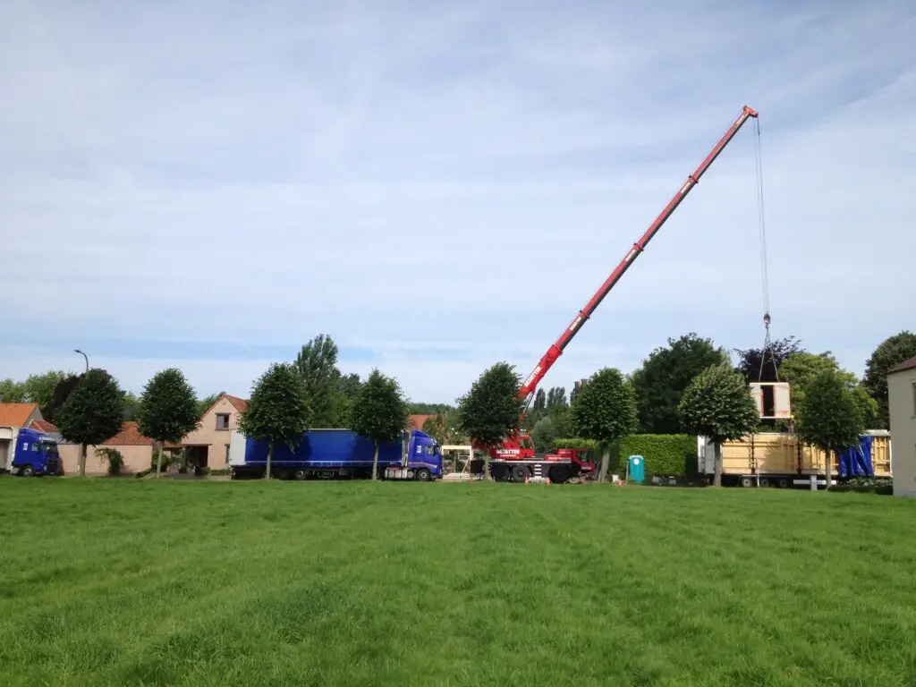 Kraan hijst een prefab houtskeletpaneel bij de nieuwbouw in Landegem