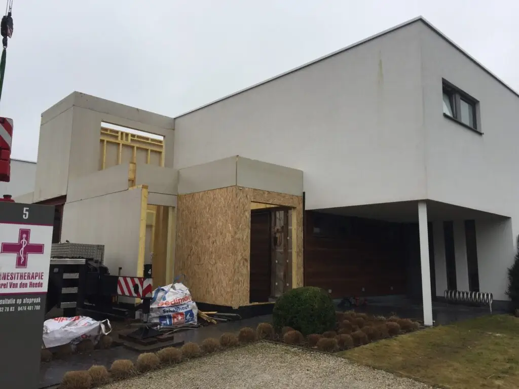Houten aanbouw met een grote opening naast de bestaande witte gevel in Waregem