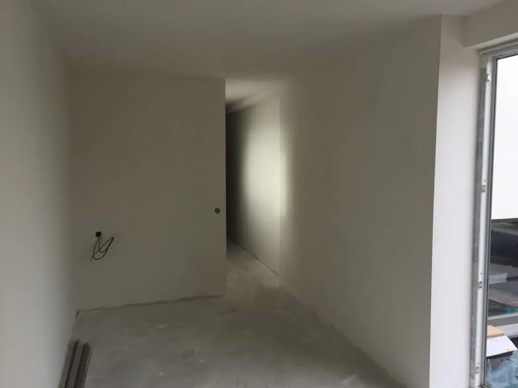 Binnenruimte van de aanbouw in Waregem met wit afgewerkte wanden en een raamopening