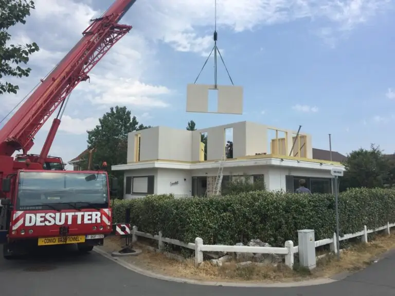 montage van prefabwand in houtskeletbouw. de wand hangt aan de kraan om te kunnen plaatsen op de bestaande woning.