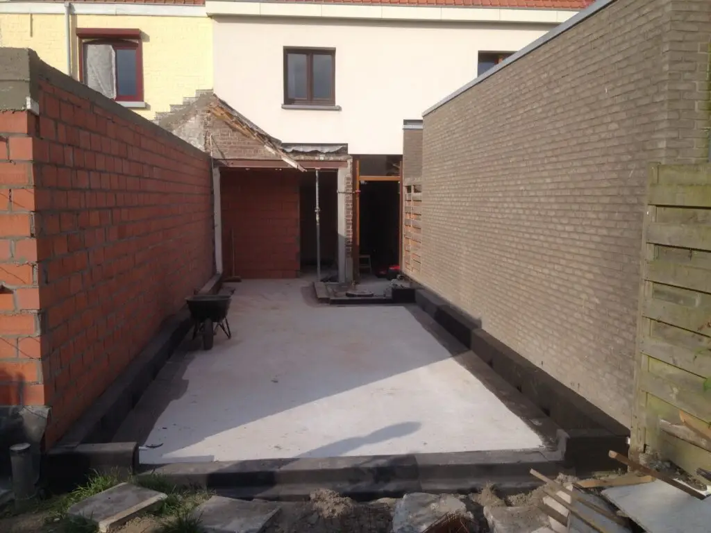 Funderingsfase van de aanbouw in Drongen tussen bestaande zijmuren en de woning
