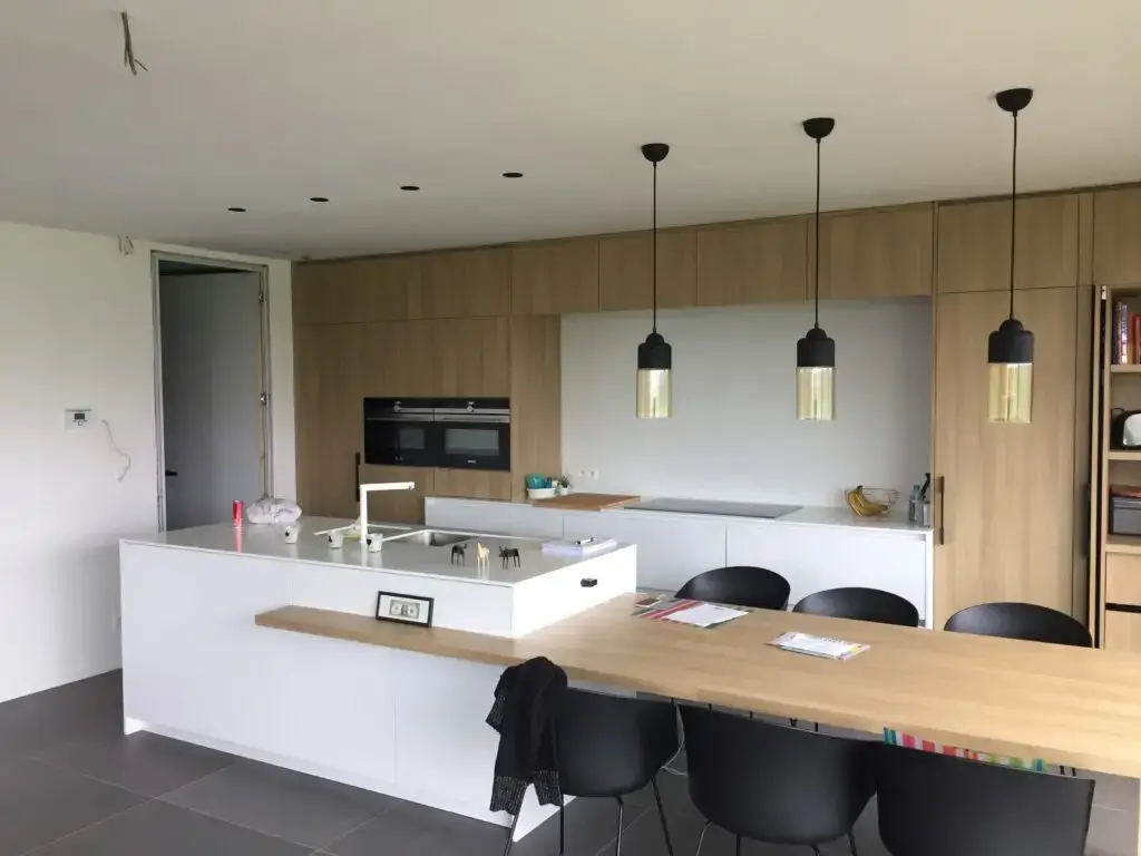 Keuken met wit kookeiland, houten kastenwand en eettafel in de woning in Heldergem
