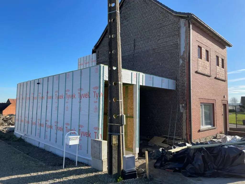 Houten carportconstructie met beschermfolie naast de bestaande bakstenen woning in Semmerzake