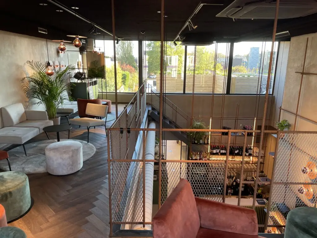 Zithoek op de verdieping met zicht op de bar en hoge ramen van LOVD in Ninove