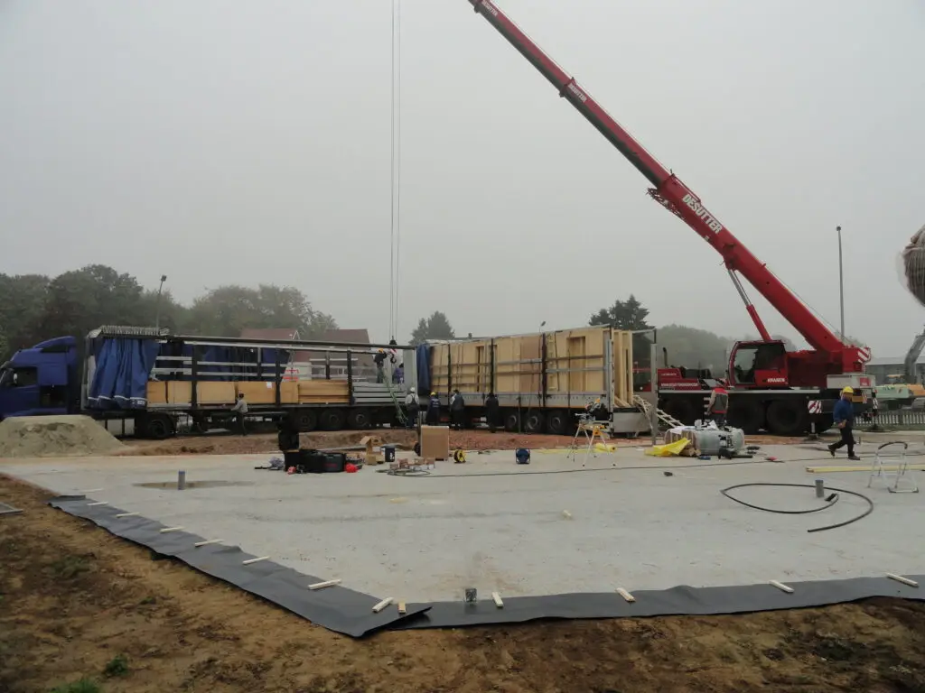 Levering van prefab houtskeletwanden met vrachtwagens en kraan op de werf van de apotheek in Zottegem
