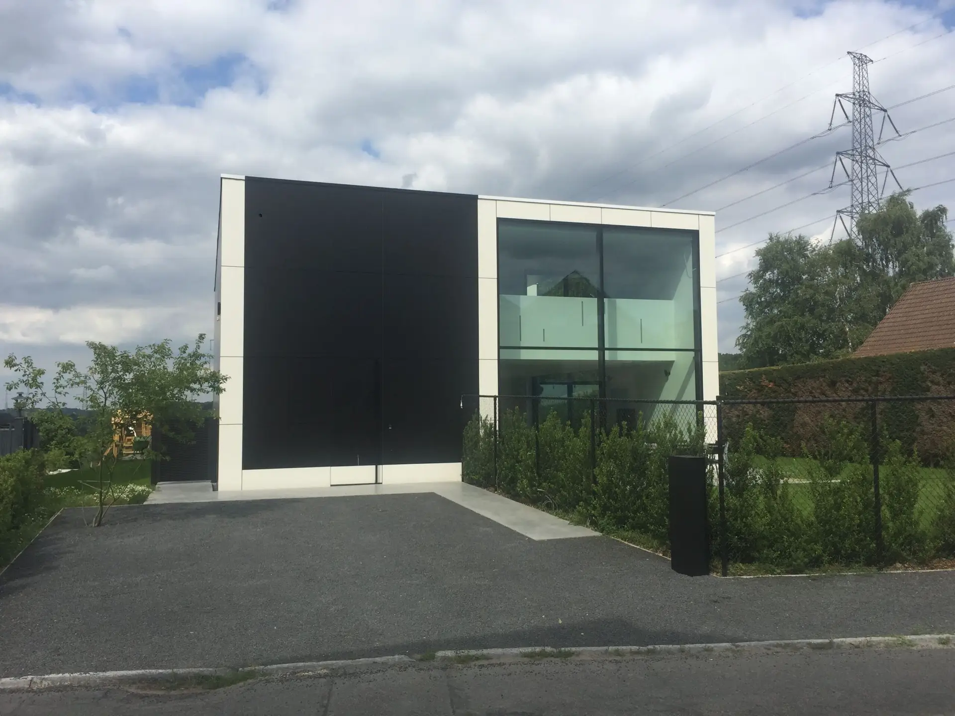 Moderne nieuwbouwwoning met donkere gevelplaten en hoge glaspartij in Dilbeek