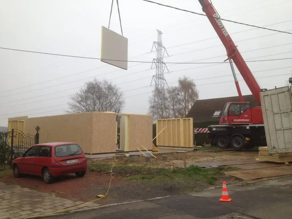 Kraan hijst een prefab houtskeletwand boven de werf in Dilbeek