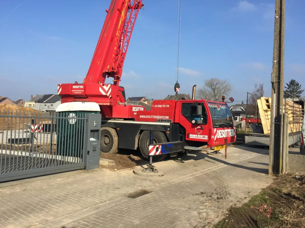 Mobiele kraan naast aangeleverde houten prefabpanelen op de werf in Haaltert