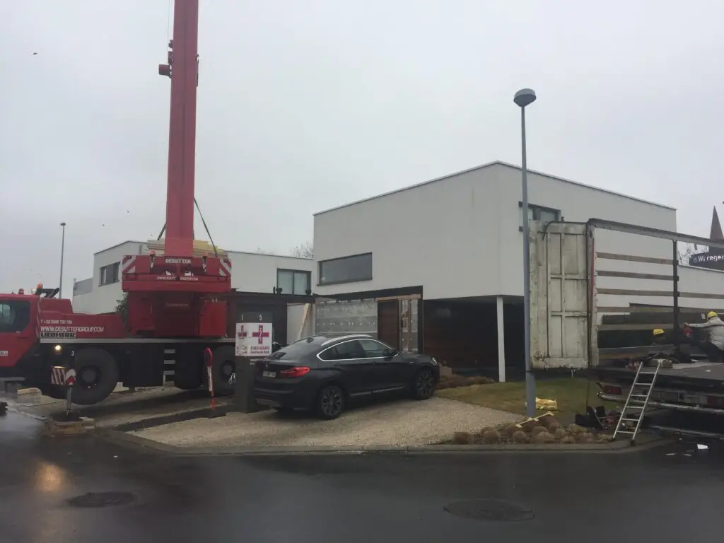 Kraanwagen voor de bestaande woning tijdens de plaatsing van de aanbouw in Waregem