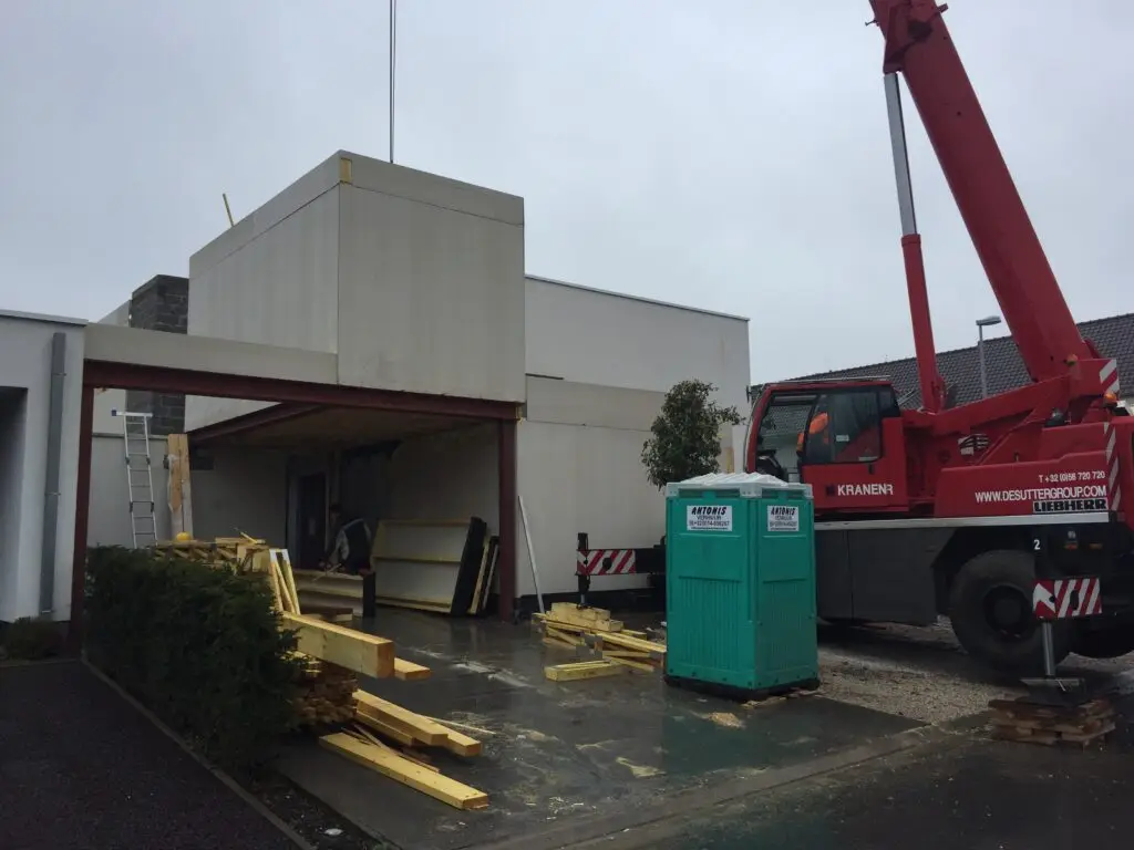 Kraan en houten constructie tijdens de montage van de aanbouw in Waregem