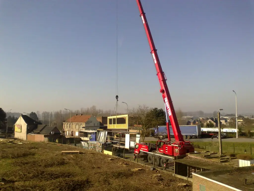 Kraan hijst een prefab houtskeletwand met raamopeningen in Ophasselt