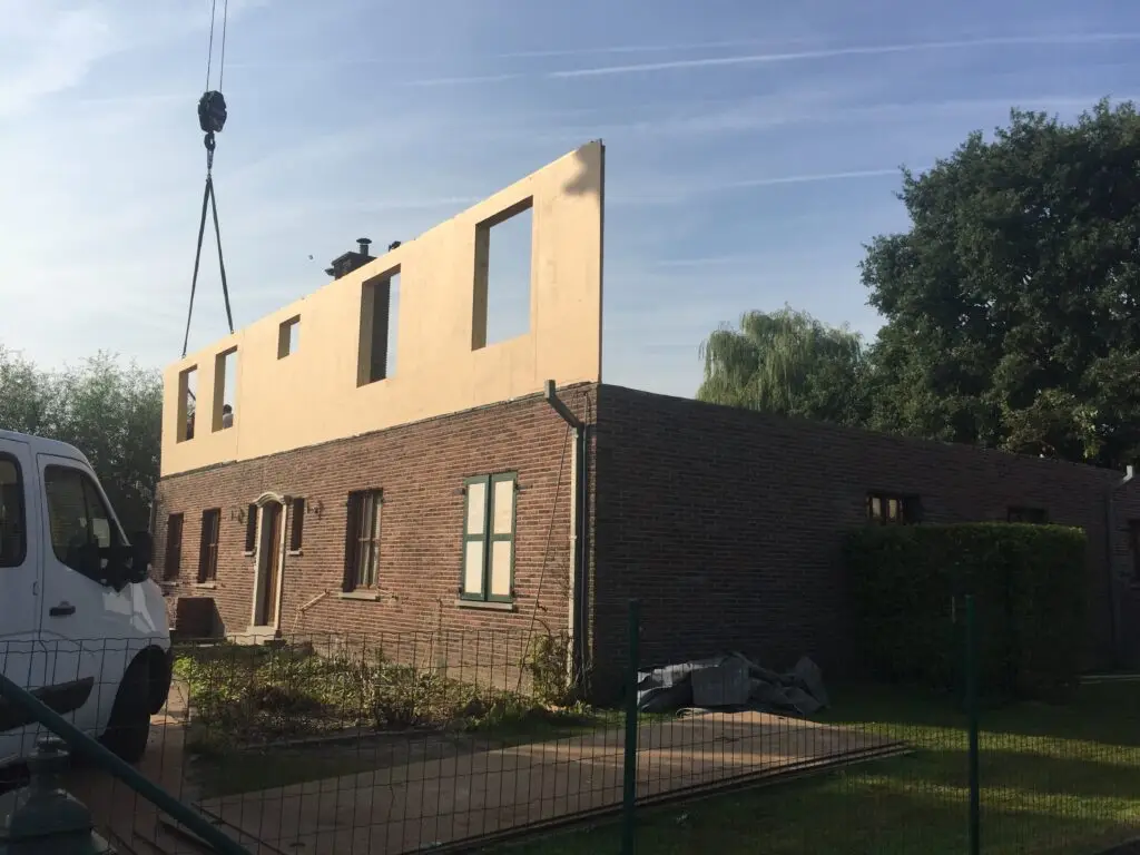 Kraan plaatst een prefab wandpaneel voor de extra verdieping op de woning in Aalter