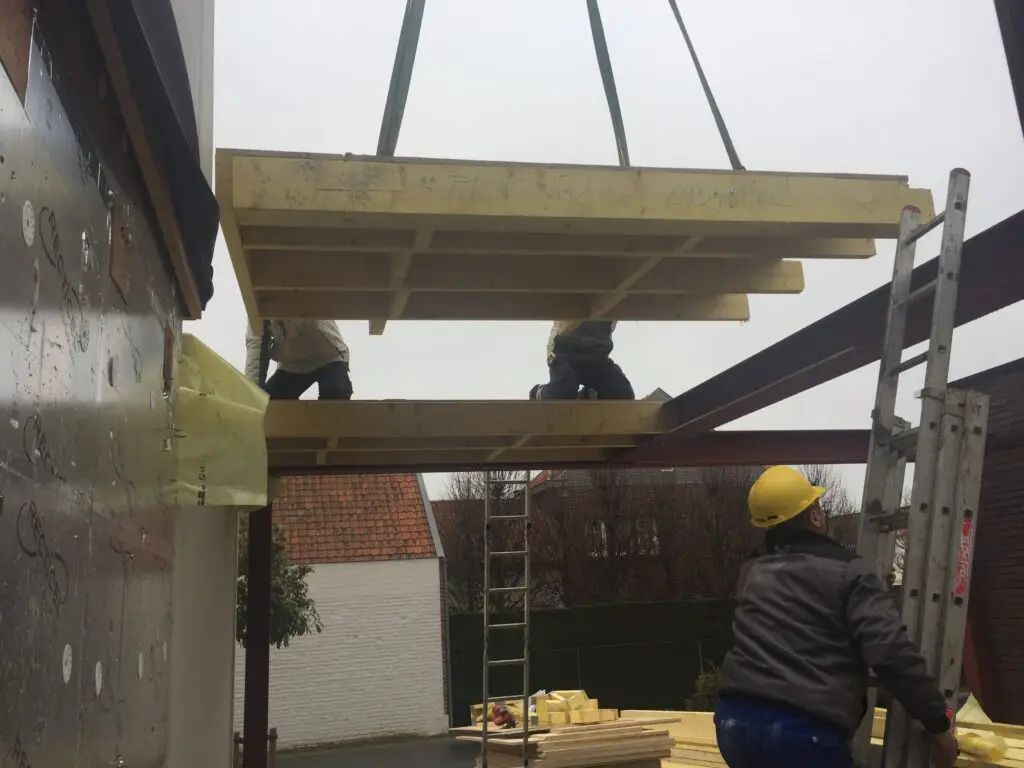 Houten vloerpaneel wordt met een kraan boven de constructie in Waregem geplaatst