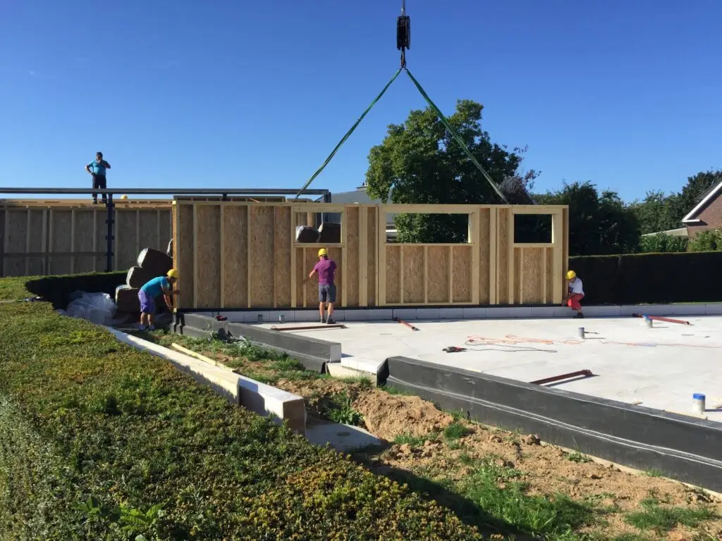 Prefab houtskeletwand aan een kraan boven de fundering van de nieuwbouw in Zottegem