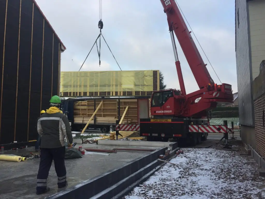 Kraan plaatst een prefab houtskeletpaneel op de werf in Voorde