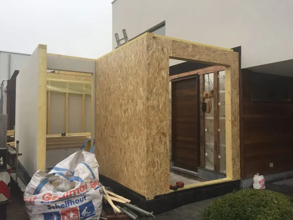 Houten wandconstructie met plaatbekleding en een deuropening bij de aanbouw in Waregem