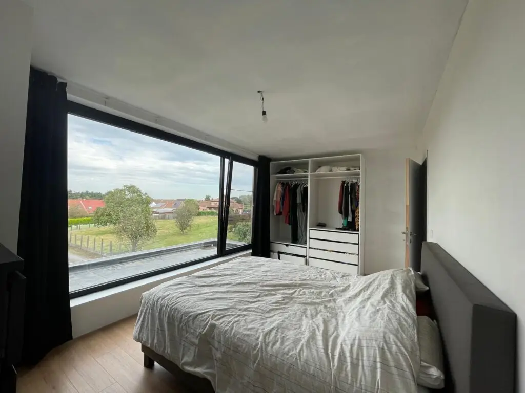 Slaapkamer met groot raam, bed en open kledingkast in de aanbouw in Semmerzake