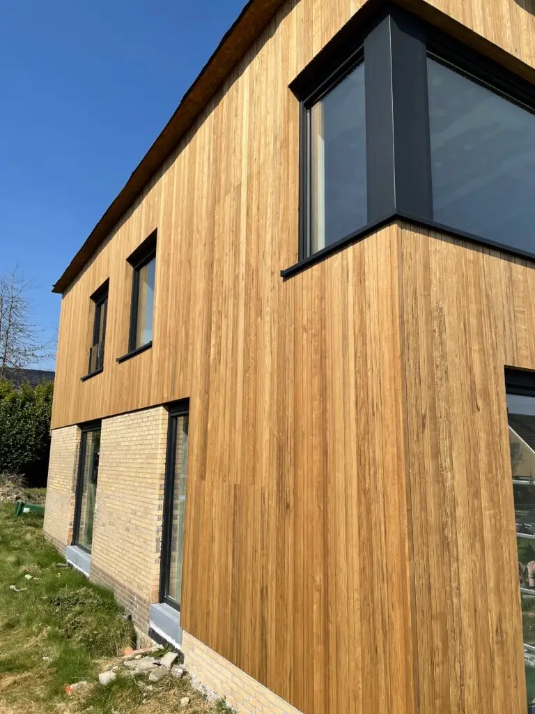 Verticale houten gevelbekleding en zwarte ramen aan de extra verdieping in Merelbeke